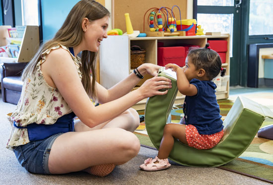 Student plays with young child on a rocking chair